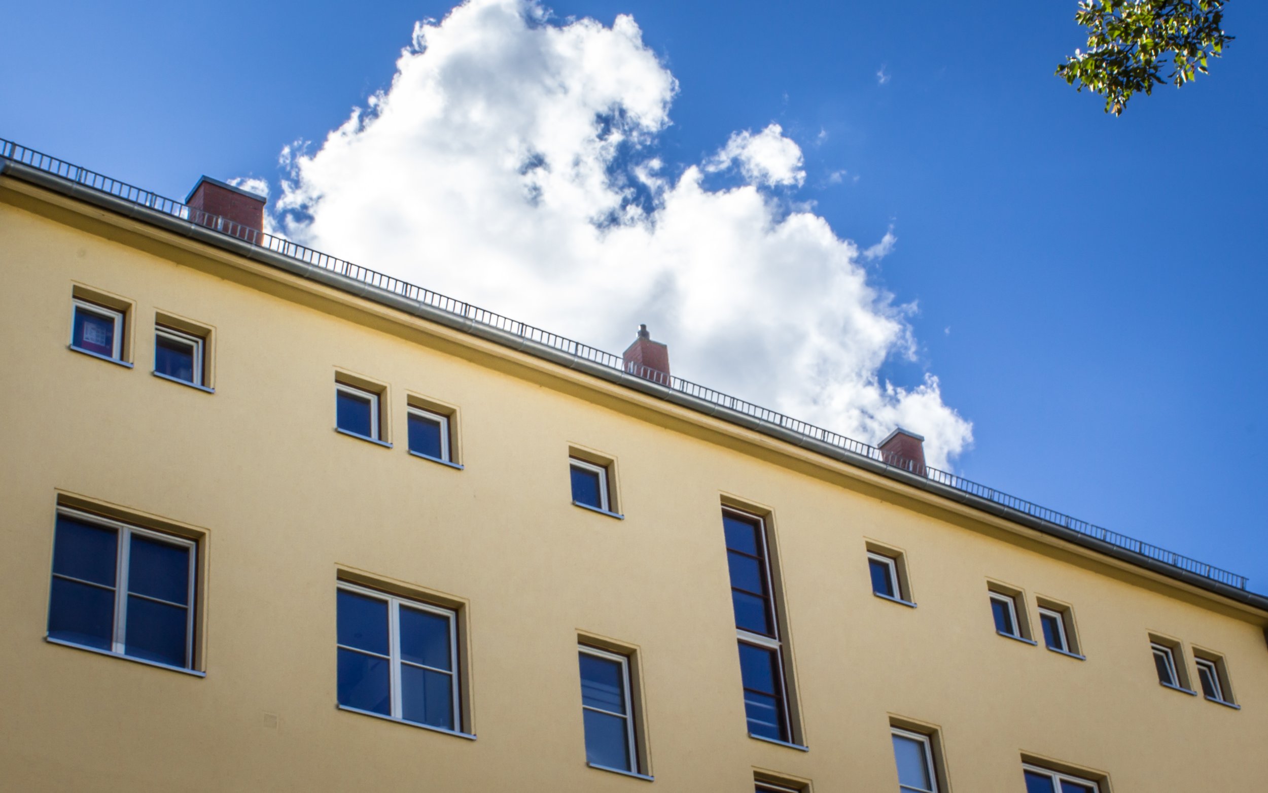 gelbe Hauswand, im Hintergrund blauer Himmel und eine große, weiße Wolke